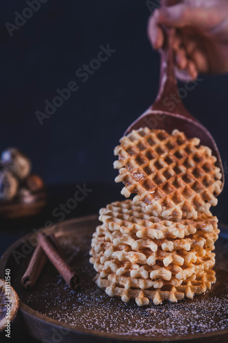 waffles are laid out on a plate. put golden toasted waffles on a plate with a wooden spatula. waffles with cinnamon and spices
