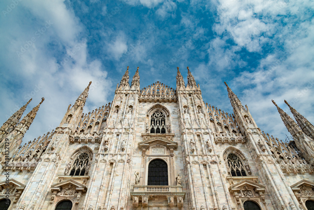 Perspective of the gothic facade of the famous Duomo di Milano (meaning: Milan's Cathedral). Blue sky and white clouds on the background.