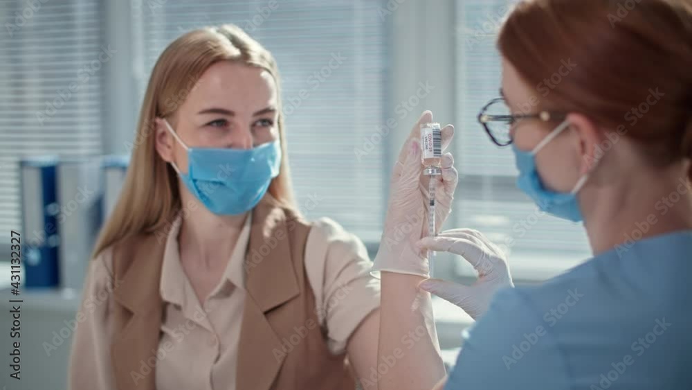 doctor uses hypodermic needle and syringe to put shot of drug as treatment to young female patient wearing medical mask doctor uses hypodermic needle and syringe to put shot of drug as treatment to young female patient wearing medical mask