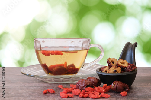 Healthy hot drink brewed from Chinese jujube and Chinese goji berries in glass and sliced Chinese date in the black cup on wooden background with  green blurred garden background. 