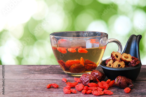 Healthy hot drink brewed from Chinese jujube and Chinese goji berries in glass and sliced Chinese date in the black cup on wooden background with  green blurred garden background. 