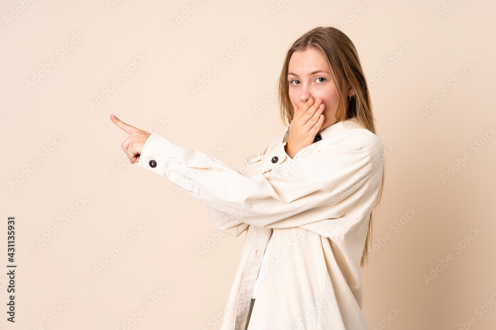 Teenager Ukrainian girl isolated on beige background with surprise expression while pointing side Teenager Ukrainian girl isolated on beige background with surprise expression while pointing side