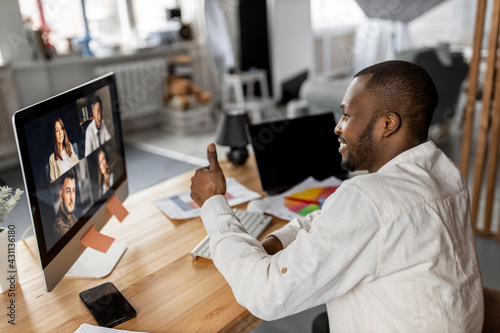 Successful businessman showing thumbs up to colleagues, coming to agreement on video meeting. African american male employee is sitting at the desk, having an online conference, remotely work concept