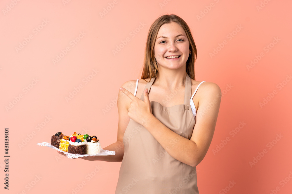 Pastry Ukrainian chef holding a muffins isolated on pink background pointing finger to the side Pastry Ukrainian chef holding a muffins isolated on pink background pointing finger to the side