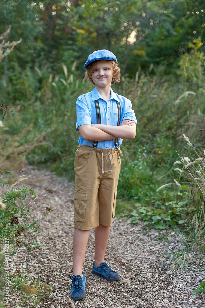 Fototapeta premium Low perspective portrait view of an attractive teenager boy sitting down with his legs crossed in a park, relaxing during a sunny day and smiling at the camera. Outdoors lifestyle