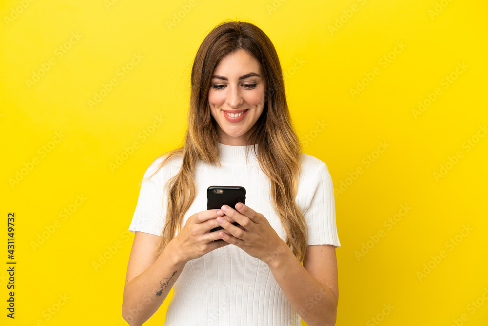 Caucasian woman isolated on yellow background sending a message or email with the mobile Caucasian woman isolated on yellow background sending a message or email with the mobile