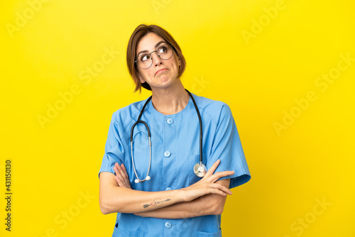 Surgeon doctor woman isolated on yellow background making doubts gesture while lifting the shoulders