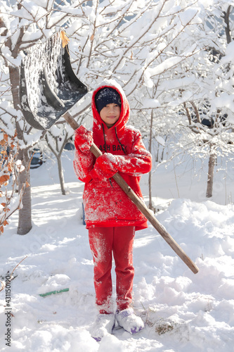 Outdoor winter portrait of a small healthy happy child with a shovel in hand.