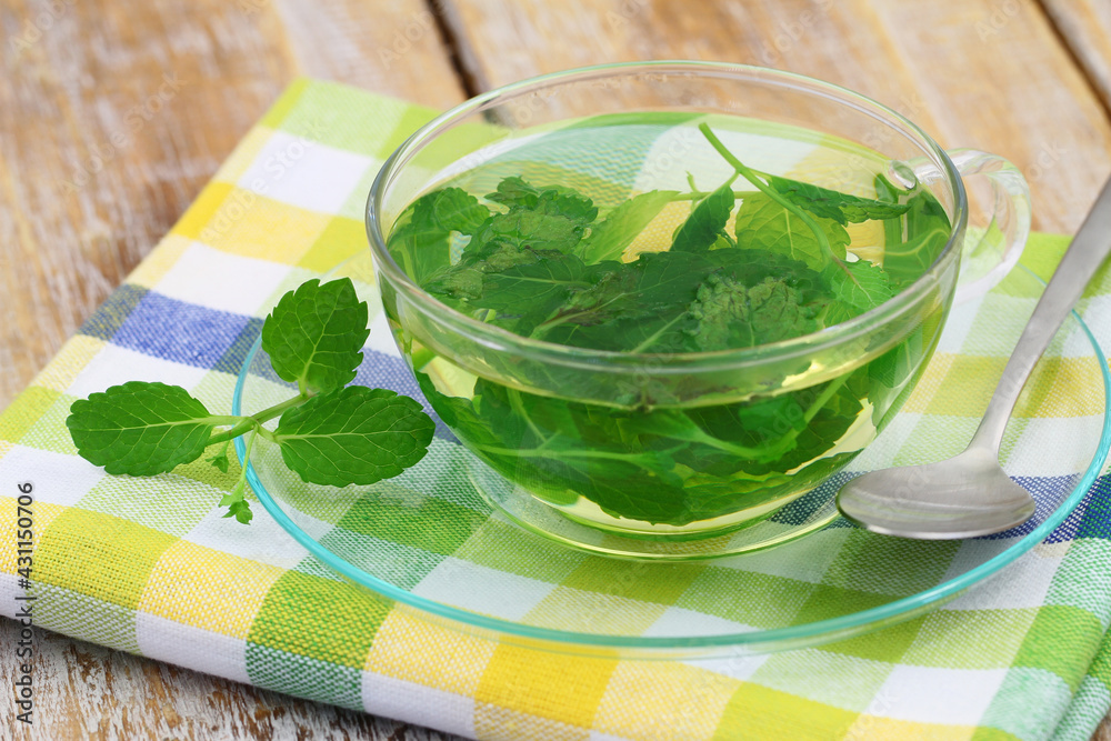 Fresh mint tea in transparent glass on checkered cloth on rustic wood