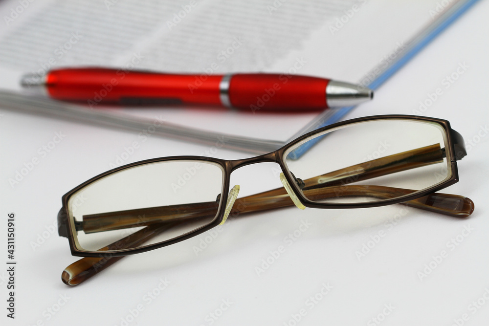 Glasses with newspaper and pen in the background
