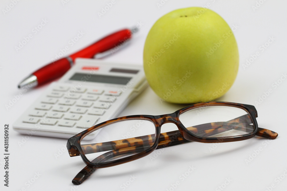 Reading glasses, calculator, pen and apple on white background