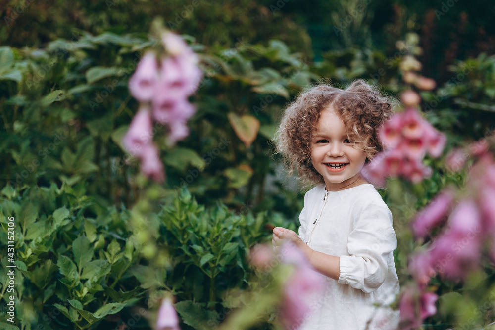 beautiful little girl with curly hair posing for photo walking among the flowers in nature beautiful little girl with curly hair posing for photo walking among the flowers in nature
