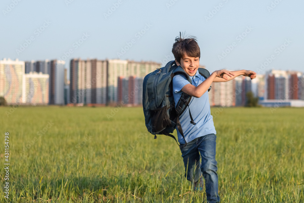 The schoolboy happily runs with a backpack on the field against the background of the city landscape The schoolboy happily runs with a backpack on the field against the background of the city landscape