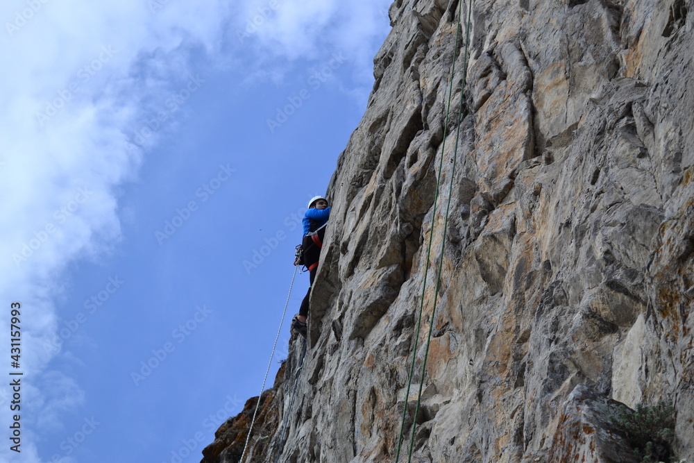 A rock climber in a white helmet climbs a rock in sunny weather