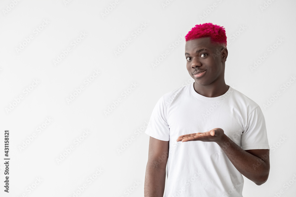 Naklejka premium Satisfied black man. Advertising product. Promotion action. Good offer. Big sale. Smiling african guy with bright pink hair white t-shirt showing copy space open palm isolated light.