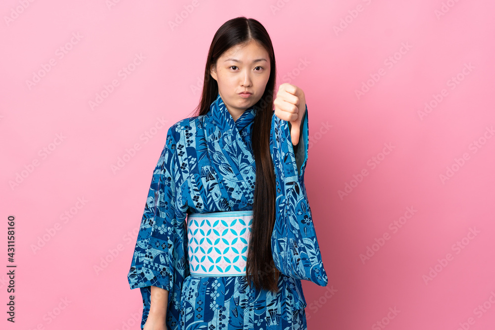 Young Chinese girl wearing kimono over isolated background showing thumb down with negative expression Young Chinese girl wearing kimono over isolated background showing thumb down with negative expression