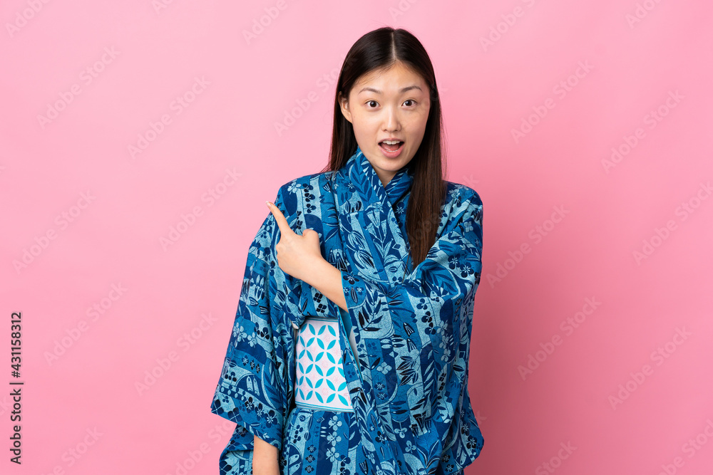Young Chinese girl wearing kimono over isolated background surprised and pointing side Young Chinese girl wearing kimono over isolated background surprised and pointing side