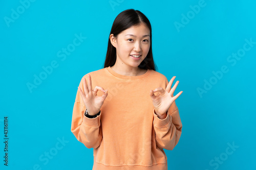 Young Chinese girl over isolated blue background showing ok sign with two hands