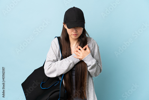 Young sport Chinese  woman with sport bag over isolated blue background having a pain in the heart © luismolinero