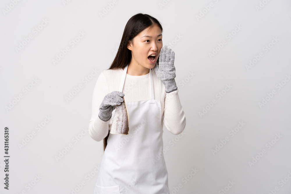 Chinese fishmonger wearing an apron and holding a raw fish over isolated white background shouting with mouth wide open to the side Chinese fishmonger wearing an apron and holding a raw fish over isolated white background shouting with mouth wide open to the side