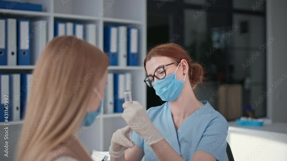charming female doctor in a medical mask is taking medicine into a syringe to vaccinate patient in hospital office