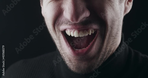 Close-up of angry laugh. Macro shot of mouth of a mad angry man smiling ominously on black background