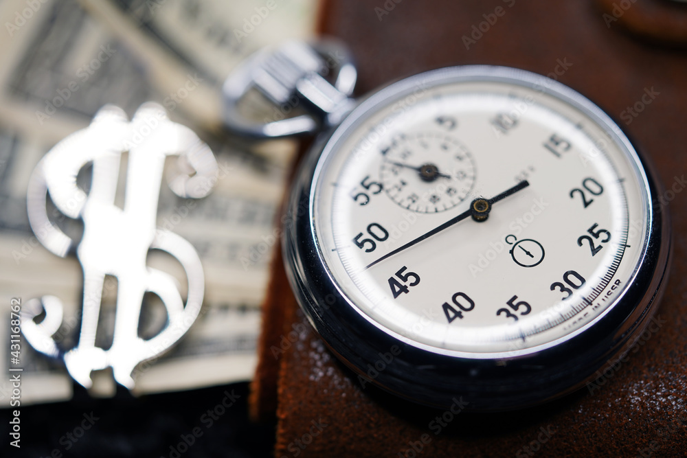 Dollar close-up. Money macro shot. The stopwatch lies on paper banknotes and a leather wallet. Clock, watch, timepiece, timer, clock face, mechanical device, speedometer Dollar close-up. Money macro shot. The stopwatch lies on paper banknotes and a leather wallet. Clock, watch, timepiece, timer, clock face, mechanical device, speedometer