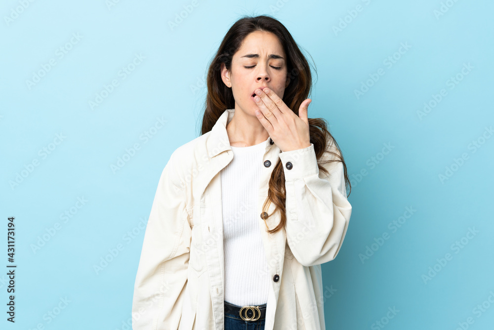 Woman over isolated background yawning and covering wide open mouth with hand Woman over isolated background yawning and covering wide open mouth with hand