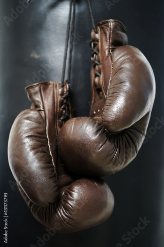 Brown leather boxing gloves lie on a black punching bag. Sport equipment. Training. The fight. Sparring                              © v75