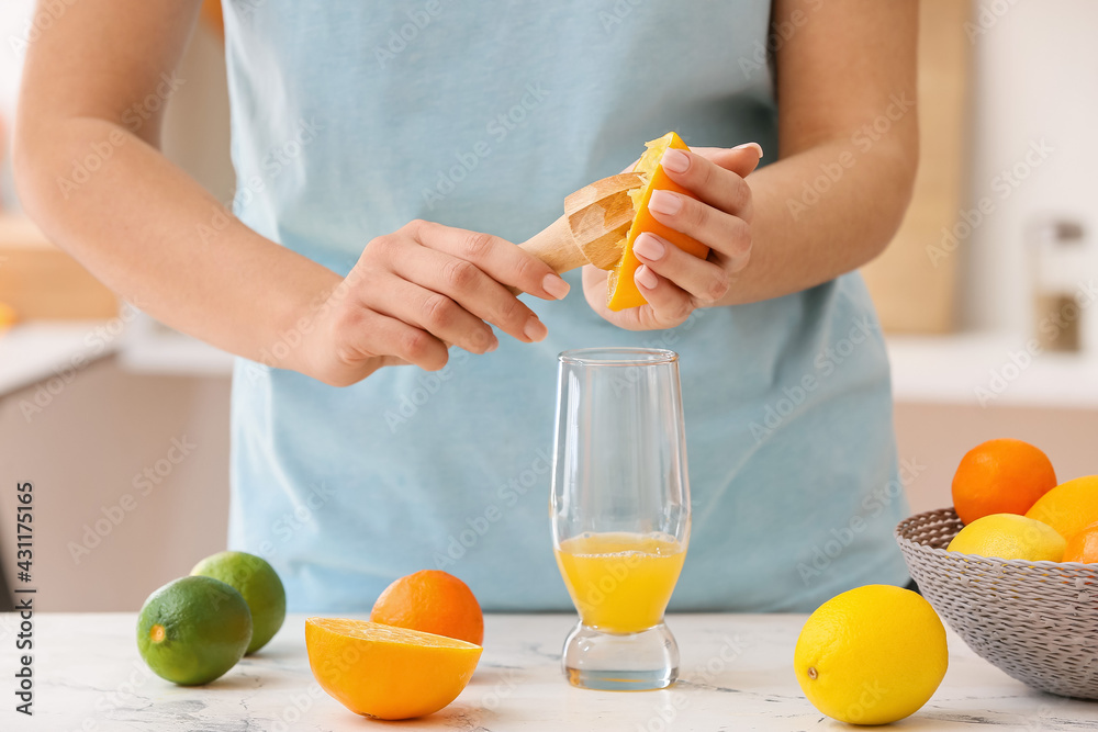 Woman making orange juice on light table in kitchen Woman making orange juice on light table in kitchen