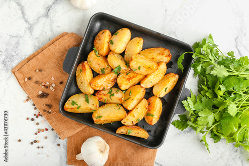 Baking sheet of tasty potatoes with parsley on light background