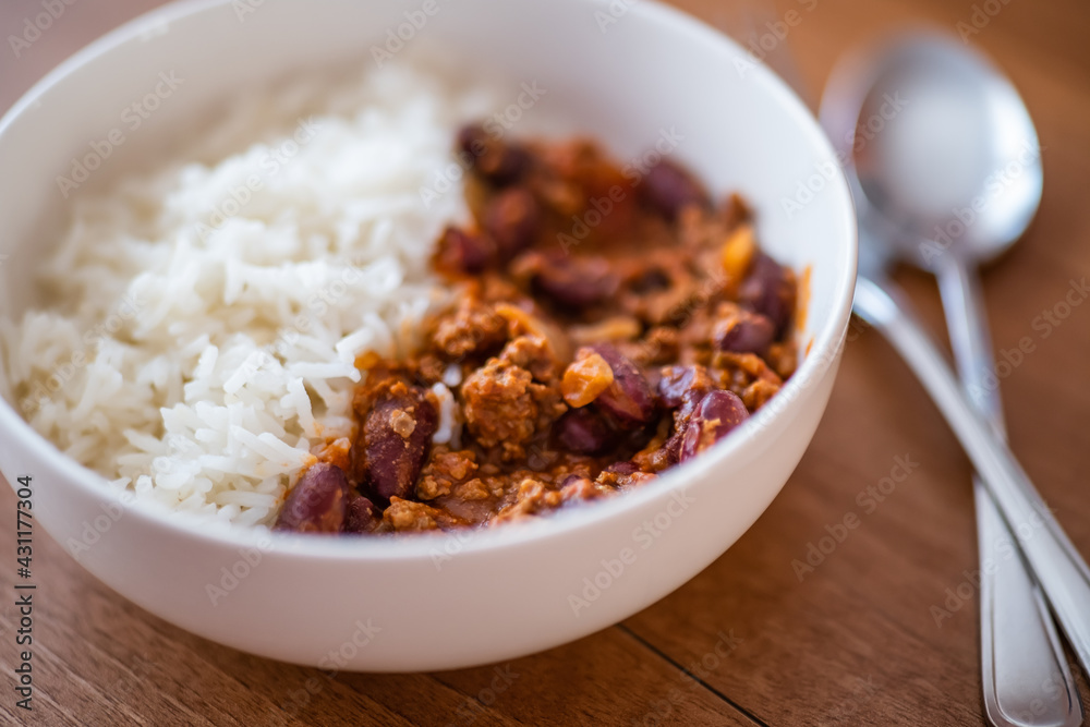 Close up and selective focus of meat chilli concarne and white rice in a white bowl on a wooden surface with intentional shallow depth of field and bokeh Close up and selective focus of meat chilli concarne and white rice in a white bowl on a wooden surface with intentional shallow depth of field and bokeh