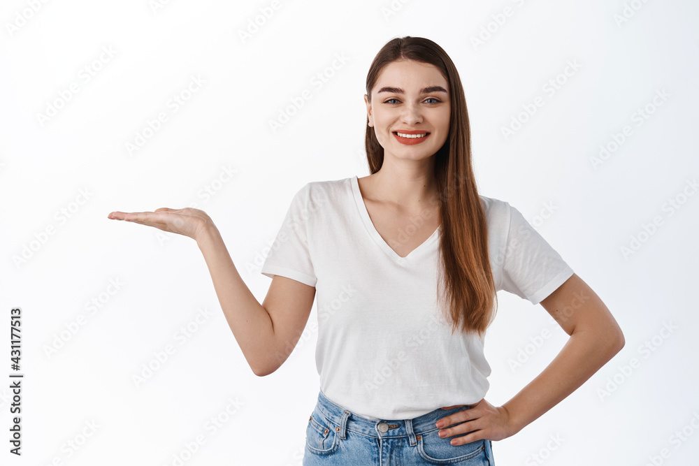 Smiling healthy girl stretch out open hand and holding your logo, promotional product, display an item on copy space, recommending buy item, standing over white background Smiling healthy girl stretch out open hand and holding your logo, promotional product, display an item on copy space, recommending buy item, standing over white background