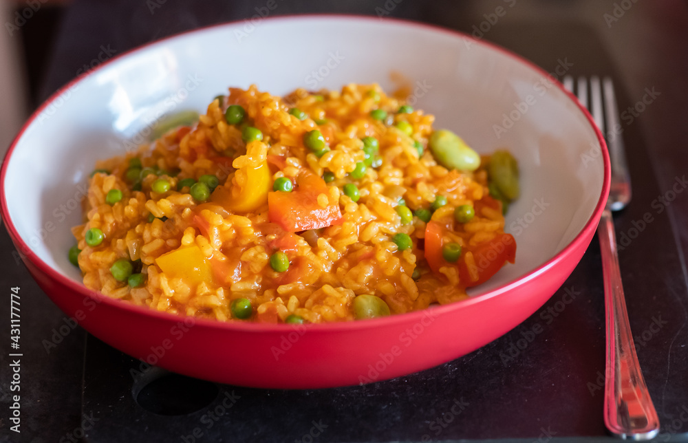 Close up of a healthy, nutritious and homemade vegetable paella in a red dinner bowl with selective focus, shallow depth of field and bokeh