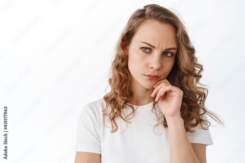 Thoughtful woman looks suspicious aside, frowning and thinking, having doubt, standing over white background Thoughtful woman looks suspicious aside, frowning and thinking, having doubt, standing over white background