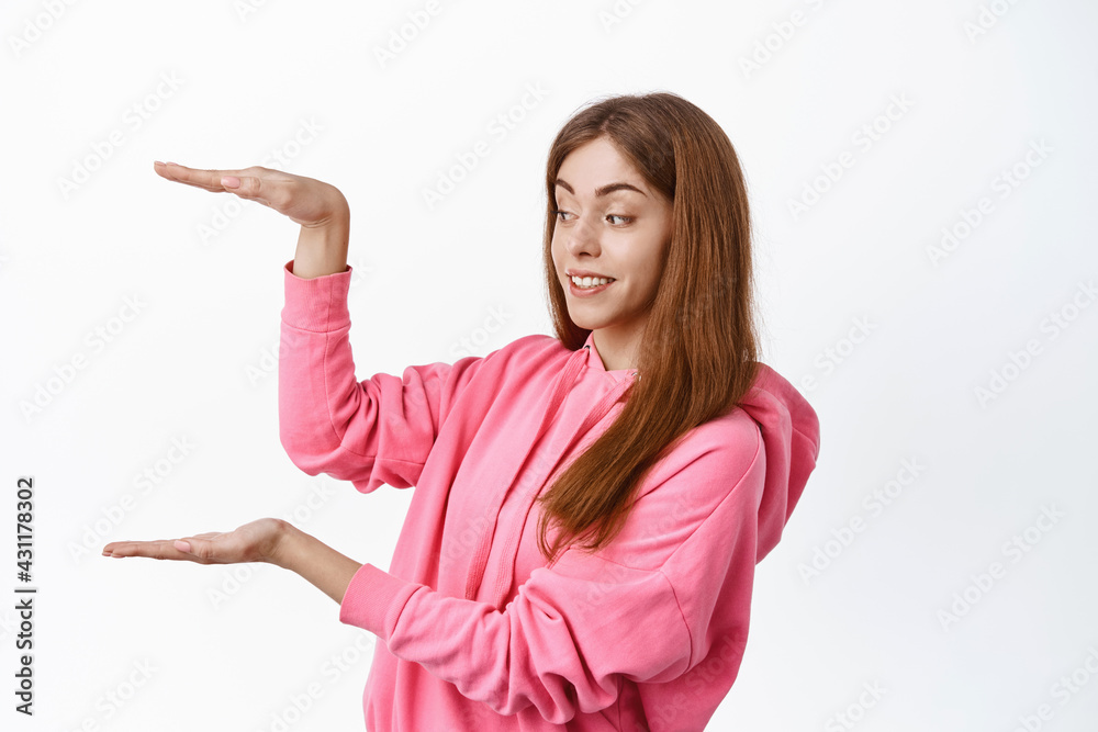 Beautiful teenage girl looking at empty space, holding empty copyspace, showing large box space, standing over white background Beautiful teenage girl looking at empty space, holding empty copyspace, showing large box space, standing over white background
