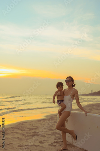 Young mother with a small child ride a S.U.P. (paddle) board in Thailand sea beach