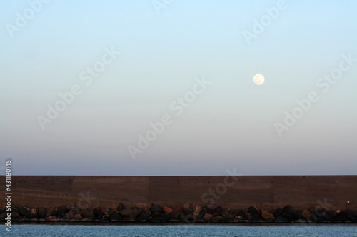 Luna che sorge da un molo di un pontile del porto di catania 