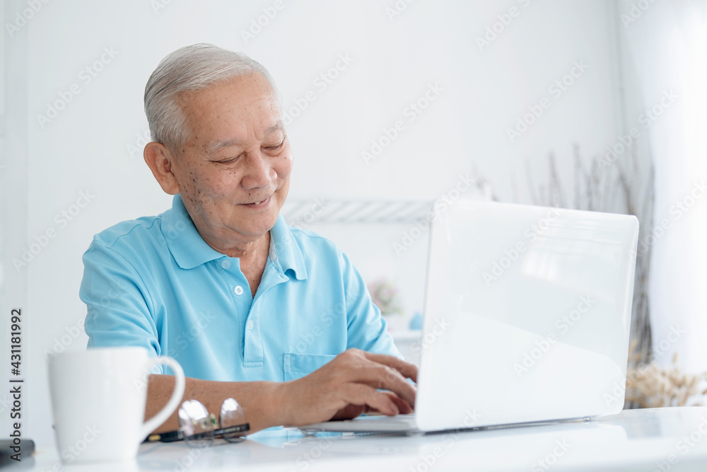 Happy senior man working on laptop and holding coffee cup