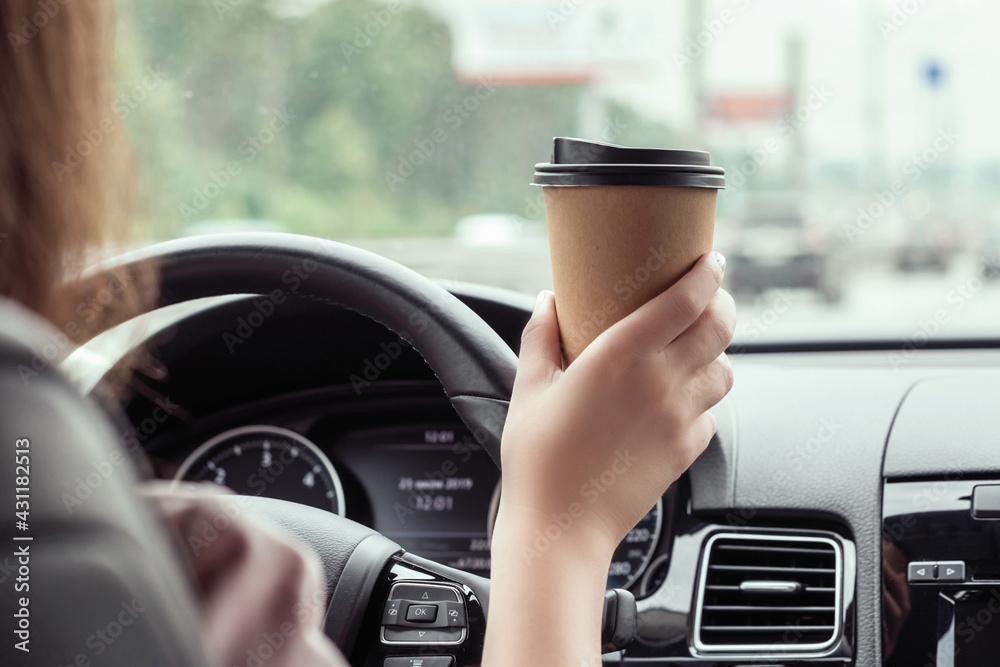 woman is driving on the highway and holding paper cup of coffee at the morning . View from the back seat of the car