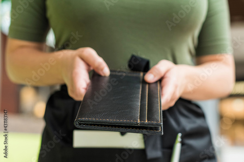 Cropped image of woman waitress in apron hold out bill folder to cafe visitor of cafe or restaurant.