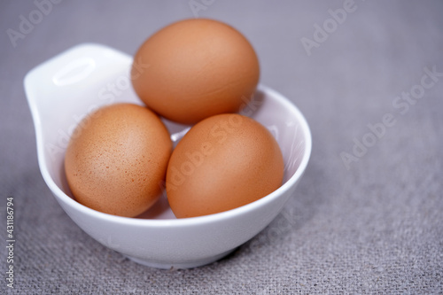 Three brown chicken eggs in a white round bowl top view. Eating raw foods. Proteins.                               