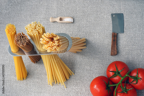 A measure of spaghetti with pasta in it, an hatchet and tomatoes lying on canvas. Cooking. Metal kitchen tools. Batch measurement. Kitchenware. Pasta. Italian Cuisine. Red 
