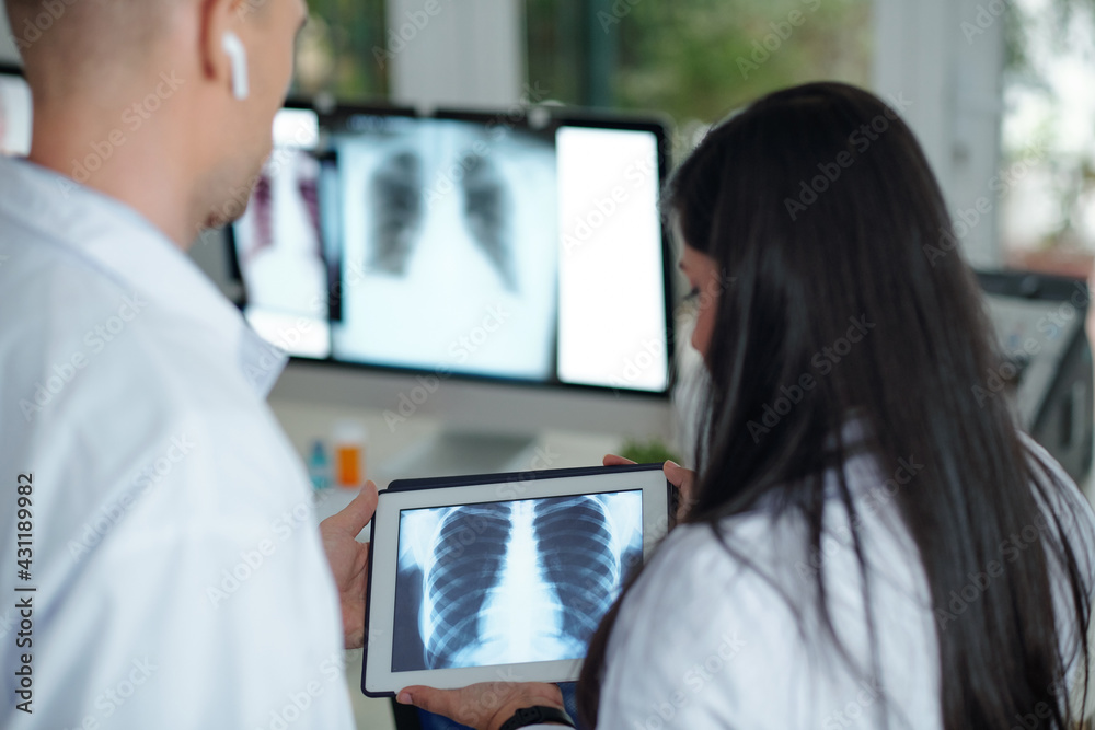 Surgeons discussing chest x-ray of patient with tumor on tablet computer, view from the back Surgeons discussing chest x-ray of patient with tumor on tablet computer, view from the back