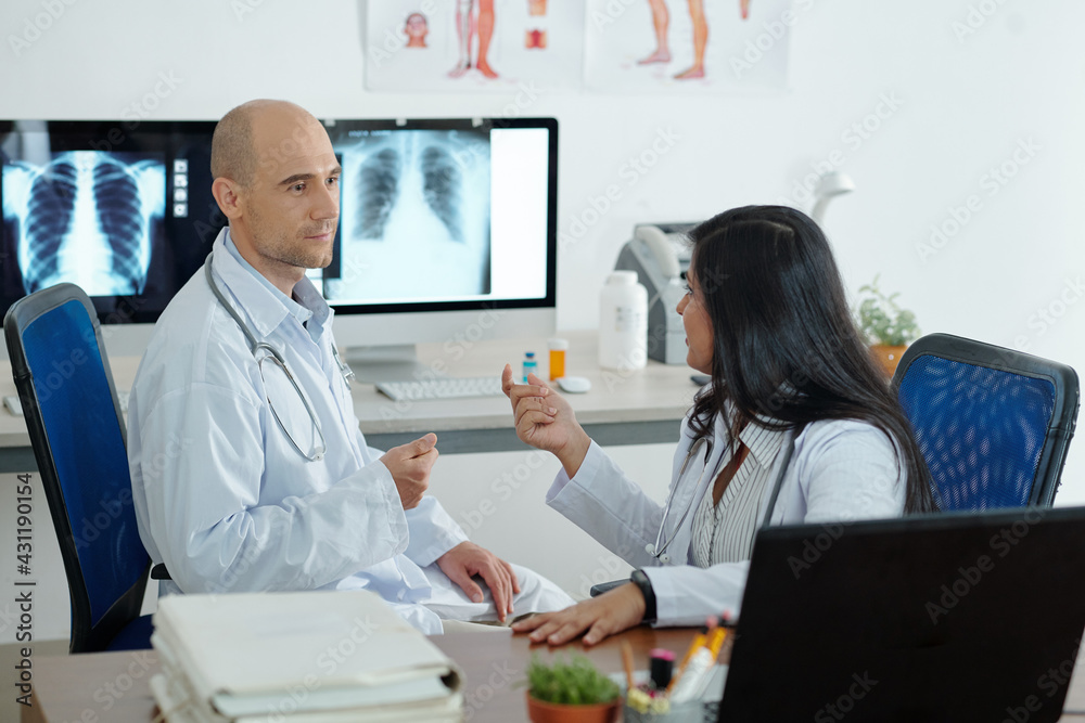 Fototapeta premium Pulmonologists discussing difficult case, they are siting in room with chest x-rays on computer screens