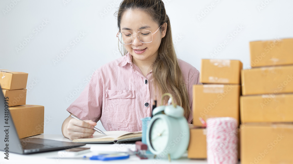 Young Asian woman is writing down the customer's details and addresses on the Clipboard in order to prepare for shipping according to the information, New kind of business for young, Sell online.