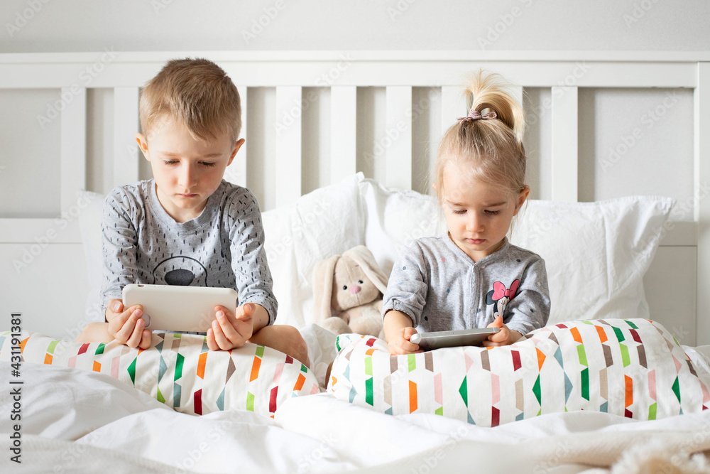 Fototapeta premium Children brother and sister watch cartoons, play on the phone, smartphone on the bed.