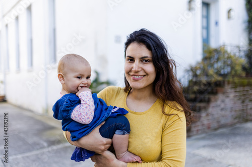 Beautiful happy mother holding her cute baby in peaceful neighborhood