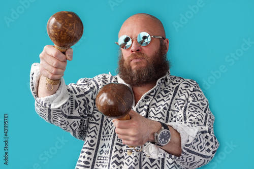 A guy with a bald head in glasses with maracas in his hands. A musician with a full beard and a mustache in a colorful shirt. Man portrait. Coconut Musical Instrument
                               