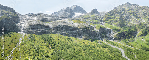 Panorama of the mountains with a cascade of waterfalls . Streams of water fall down from the green slopes .